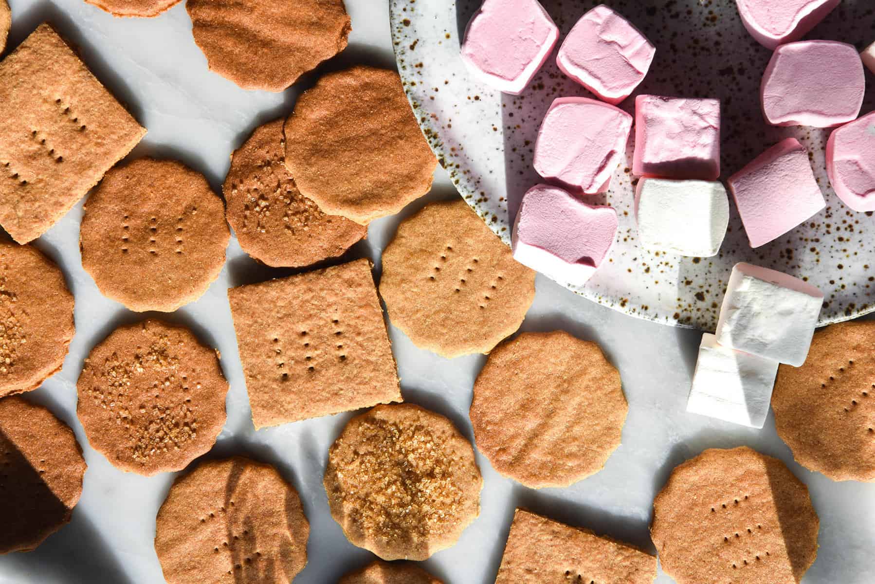 An aerial image of gluten free graham crackers with strawberry and white marshmallows atop a white marble table
