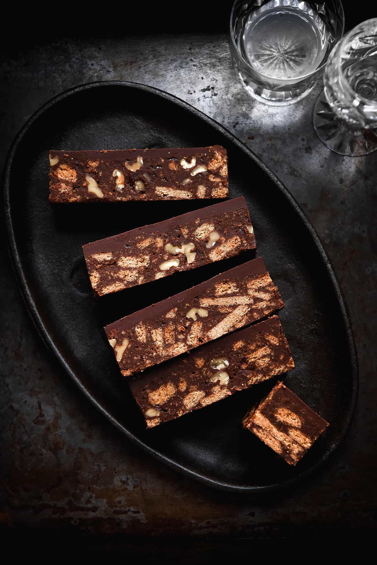 A moody aerial shot of slices of gluten free Hedgehog slice on a dark steel plate against a dark backdrop