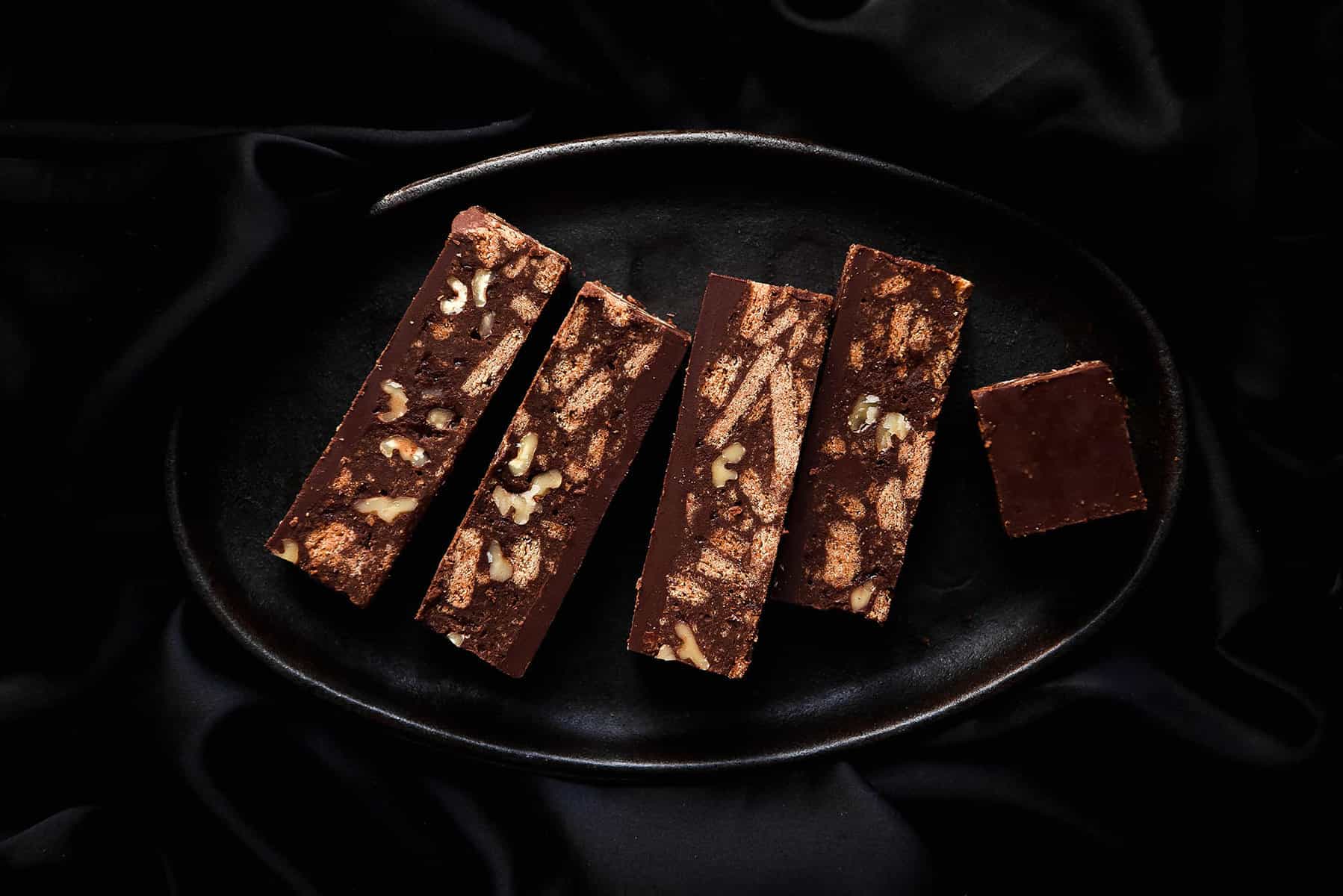 A moody aerial shot of slices of gluten free Hedgehog slice on a dark steel plate against a dark backdrop