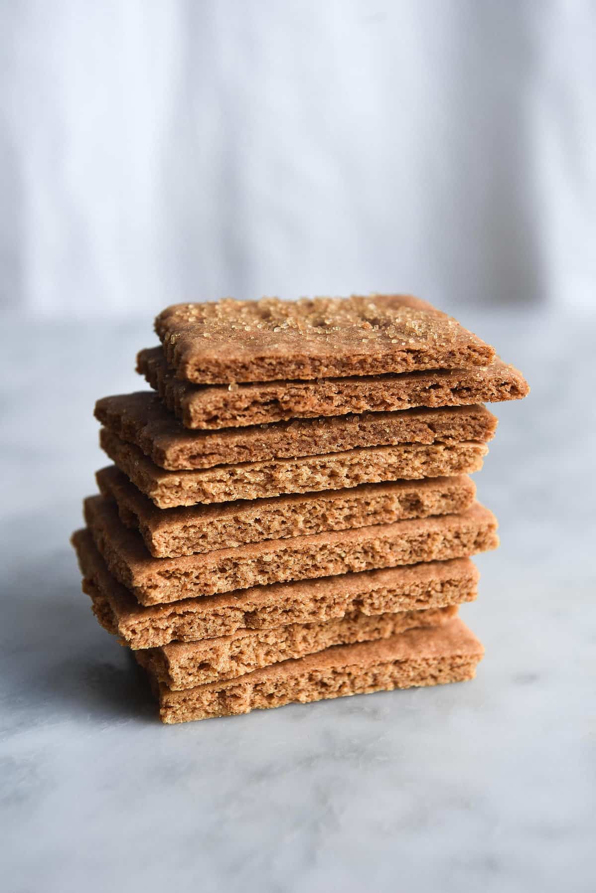 Gluten free, vegan graham crackers in a stack on a white marble table against a white linen backdrop.