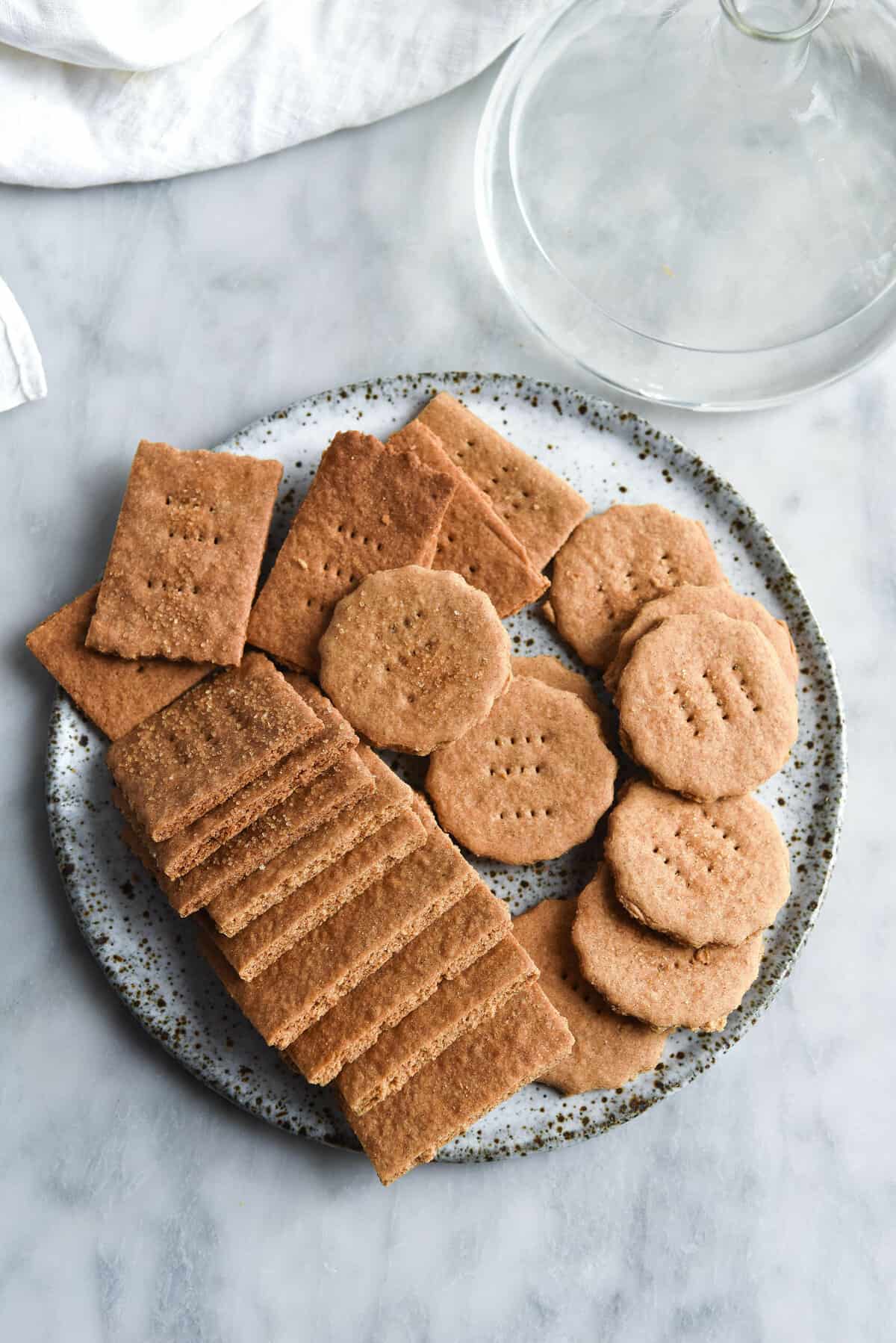 An aerial image of gluten free vegan Graham crackers on a white speckled ceramic plate atop a white marble table.