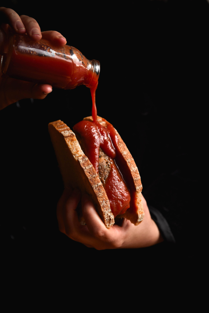 A gluten free, vegan sausage in bread with tomato sauce being poured down the side of it