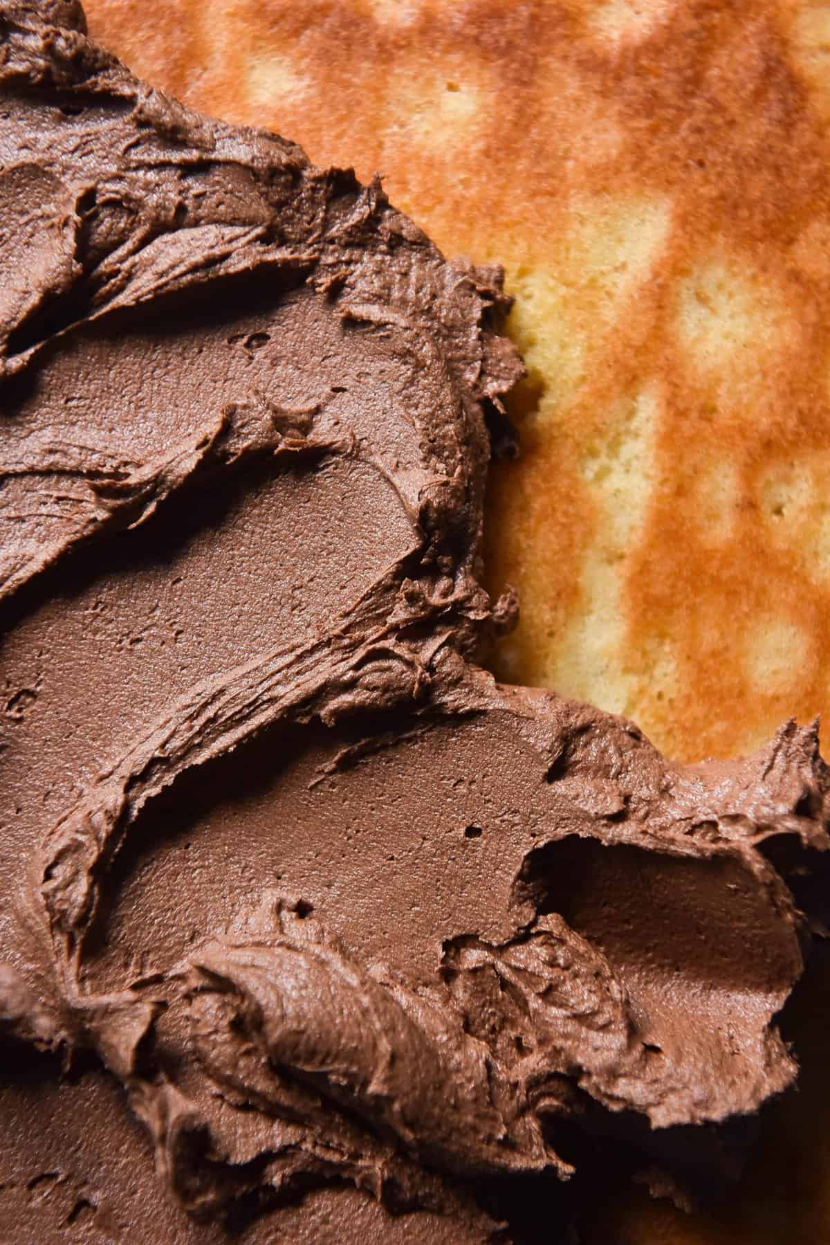 An aerial macro image of a vanilla cake half topped with brown butter chocolate buttercream swirls. 