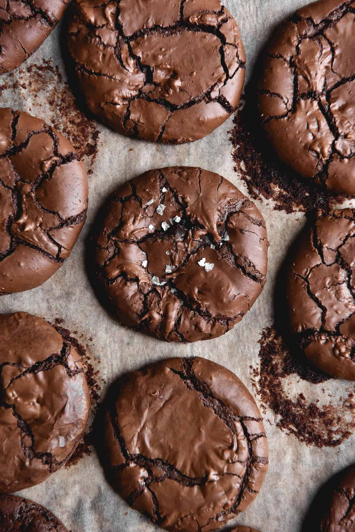 An aerial image of gluten free brownie cookies on a baking tray. The cookies are fudgy with crinkled tops and finished with a small pinch of sea salt flakes.