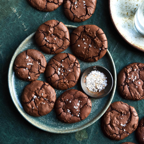 An aerial view of flourless brownie cookies atop a green plate on an olive green backdrop.