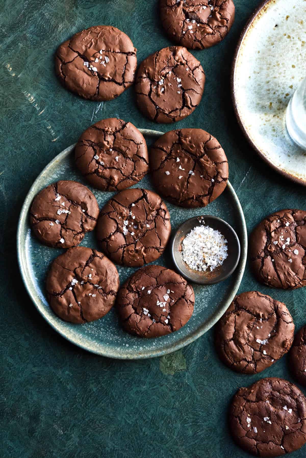 An aerial view of flourless brownie cookies atop a green plate on an olive green backdrop.