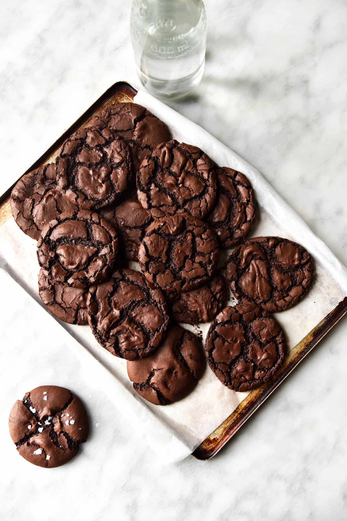 Vegan, gluten free brownie cookies on a baking tray atop a white marble table.