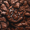 An aerial close up view of a stack of gluten free vegan brownie cookies. The brownie cookies are shiny and crackled and the centre cookie is sprinkled with sea salt flakes