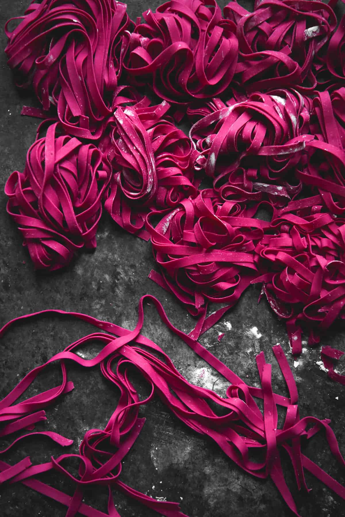 Gluten free beetroot pasta arranged in small nests on a dark blue background