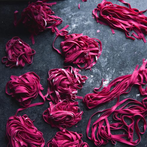 A dark and moody image of gluten free beetroot pasta dough nests on a dark blue backdrop
