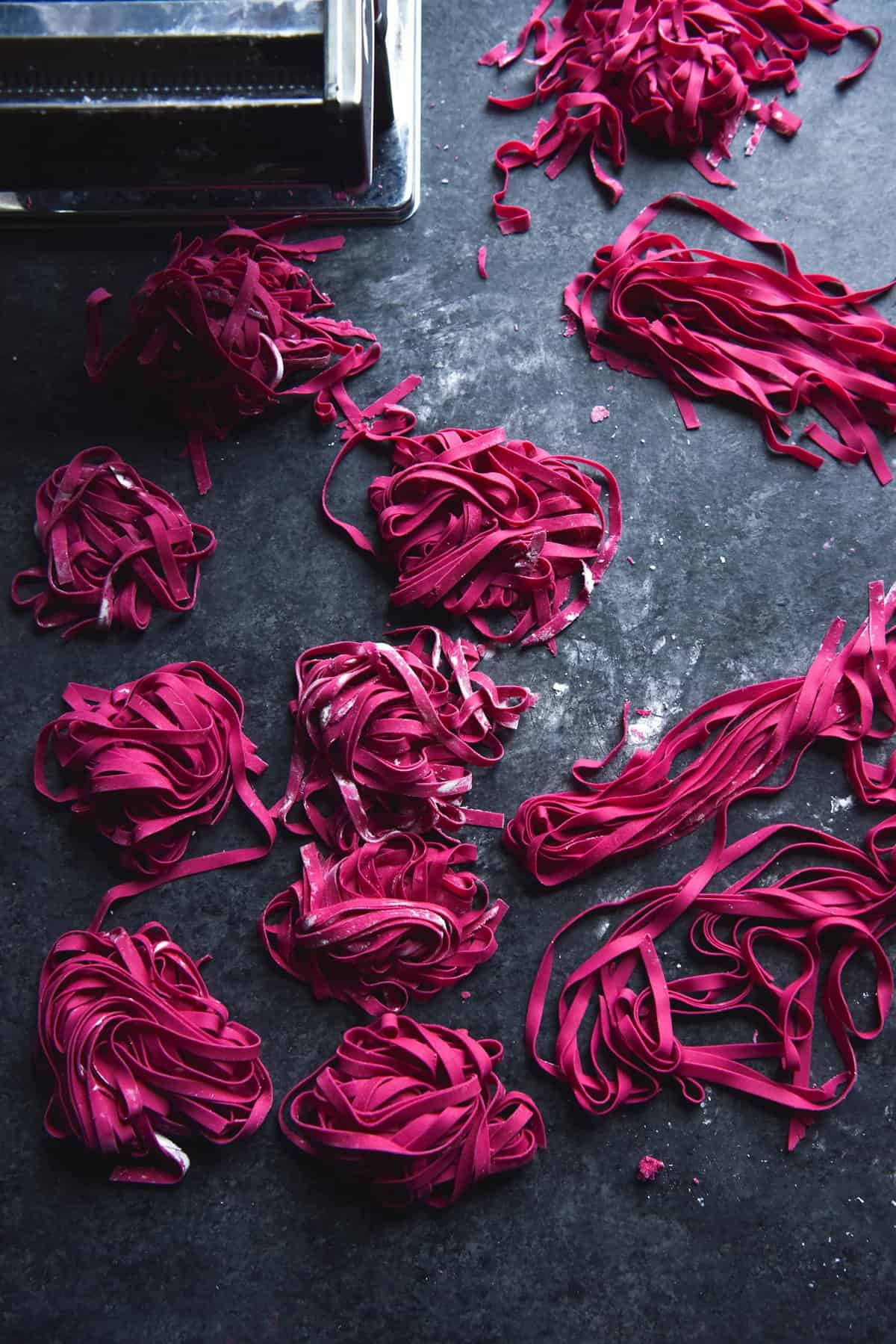 A dark and moody image of gluten free beetroot pasta dough nests on a dark blue backdrop