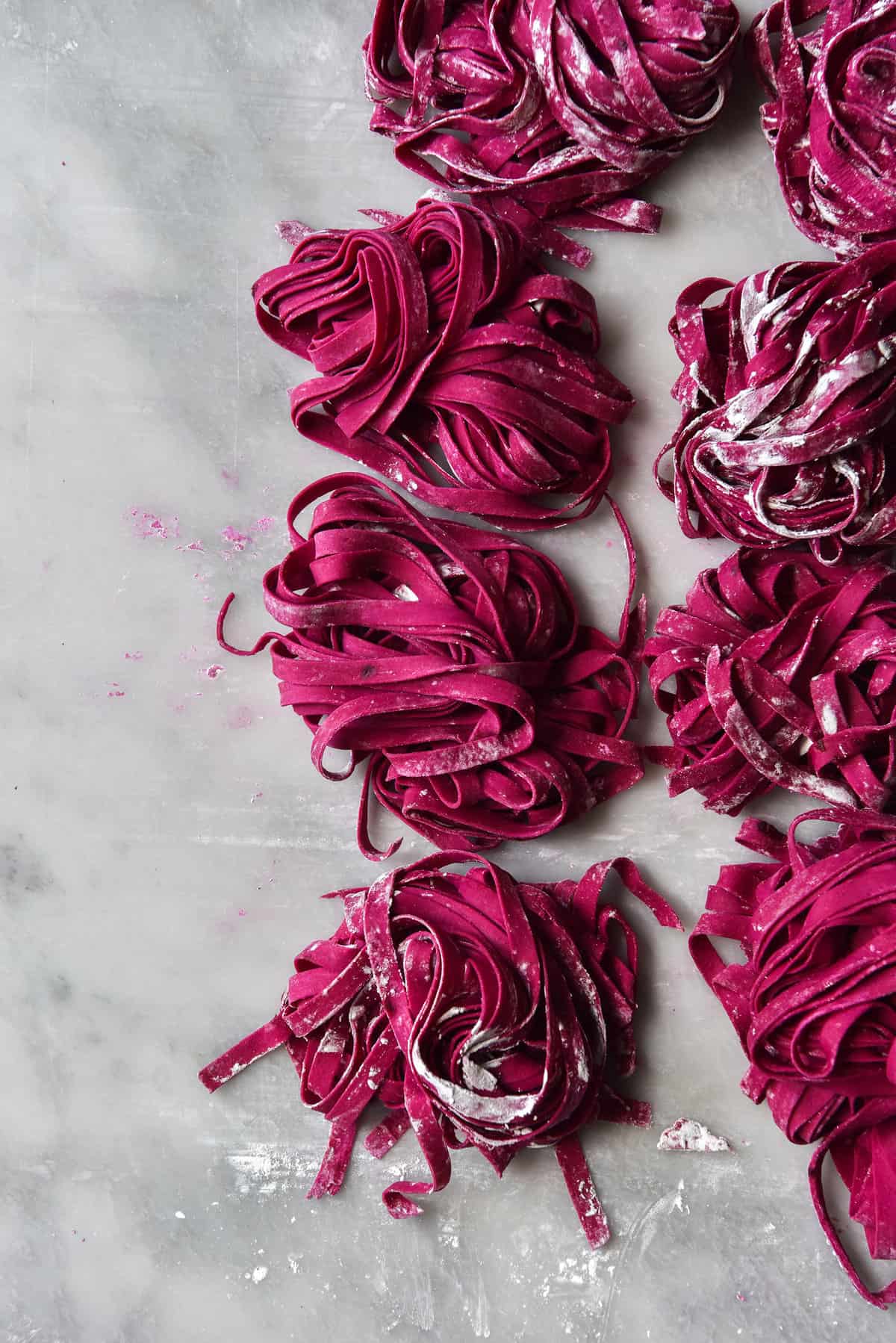 Gluten-free beetroot pasta arranged in nests atop a white marble backdrop.