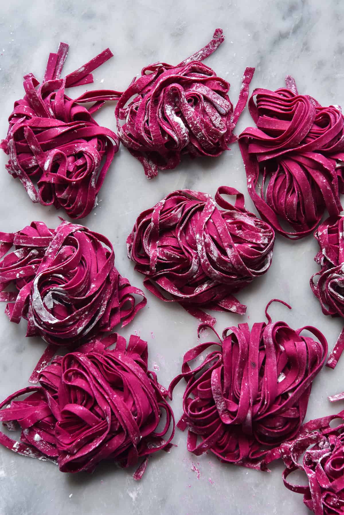 Gluten-free beetroot pasta arranged in nests on a white marble table.