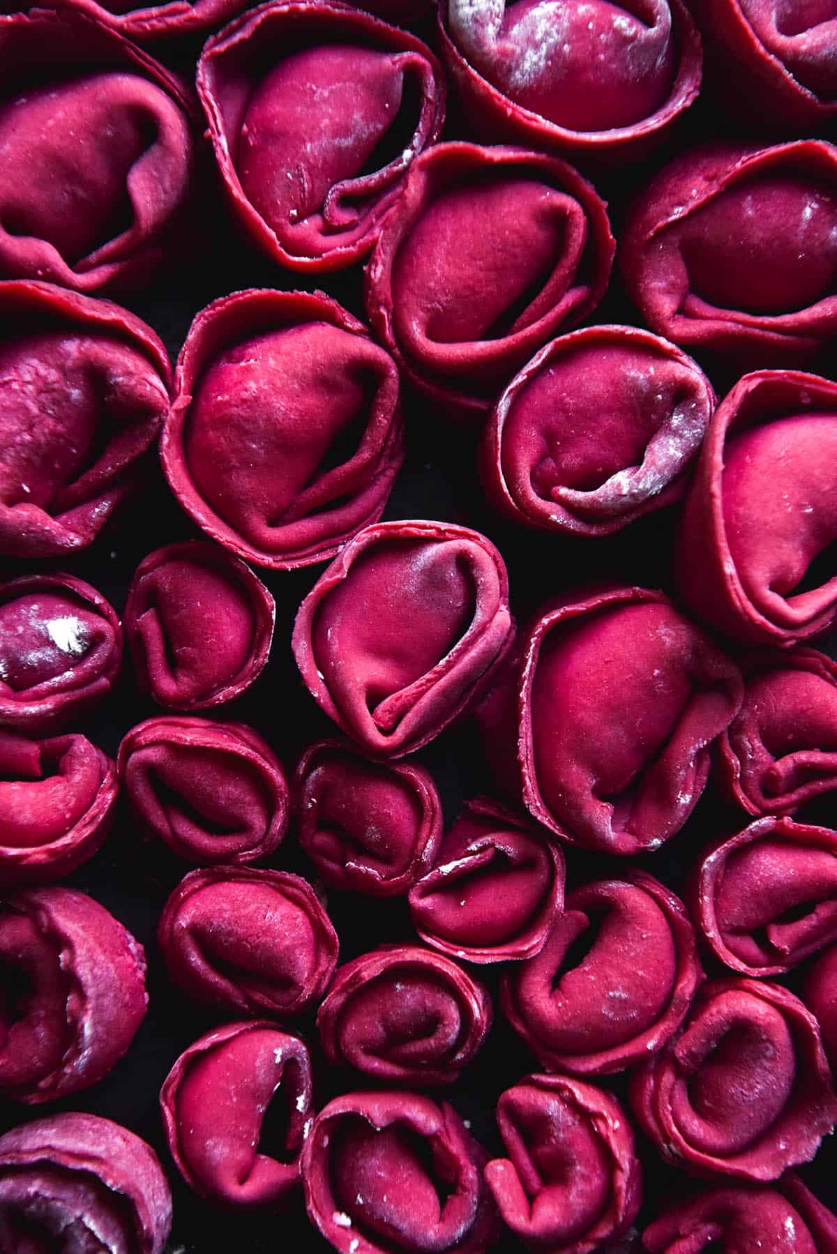 An aerial close of a tray of uncooked gluten free ravioli made from a beetroot dough. The dough is a vibrant red purple.