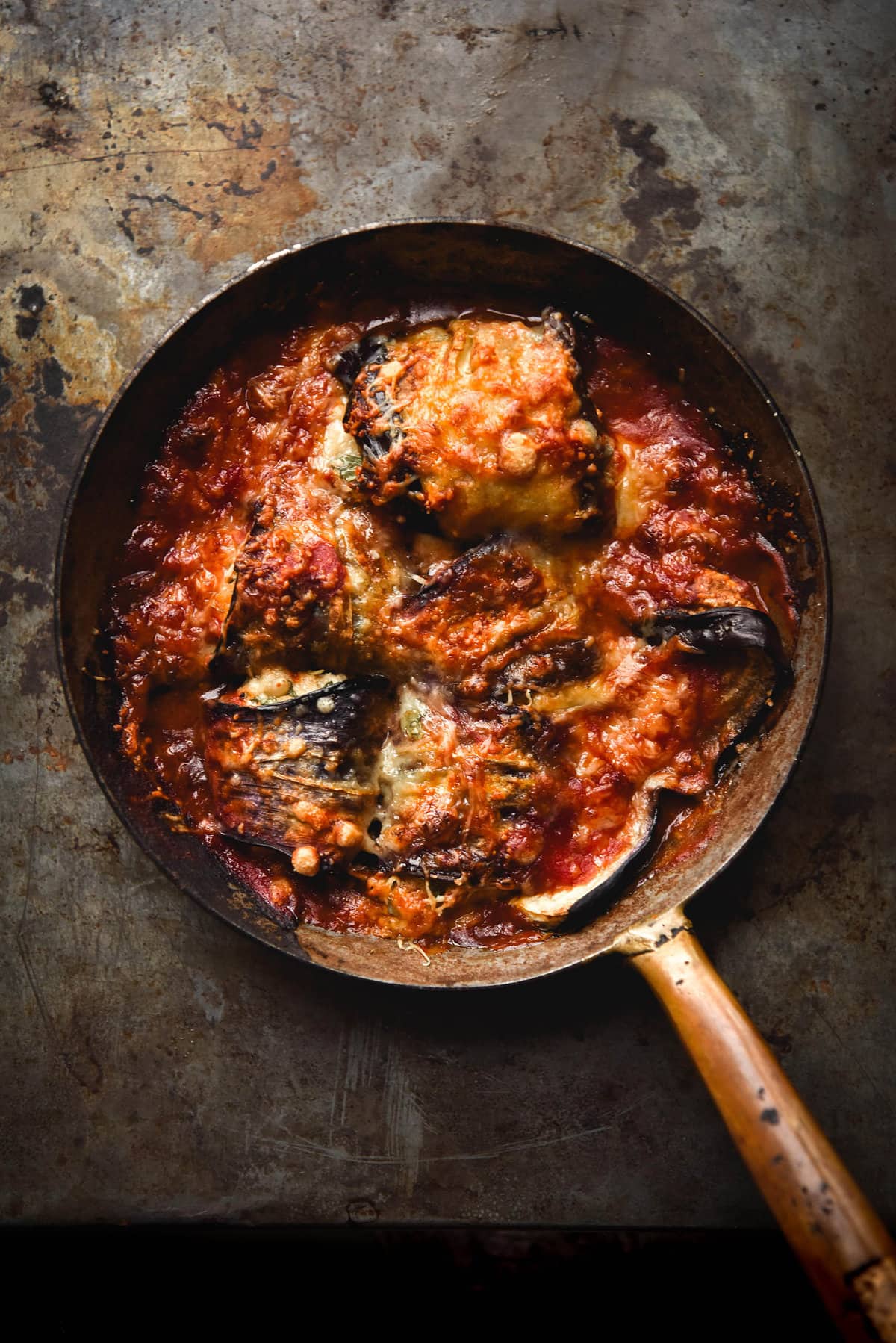 A small skillet filled with vegan sausage involtini against a dark and moody backdrop