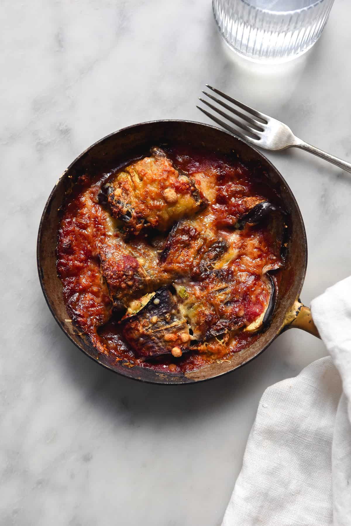 A small skillet of vegan sausage stuffed involtini on a white marble backdrop