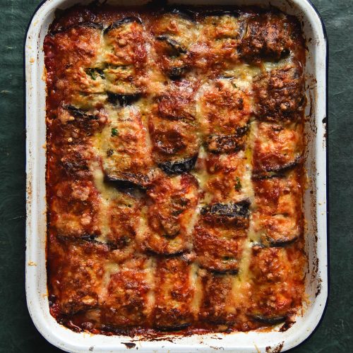 A tray of vegan sausage involtini topped with melty cheese against a green backdrop