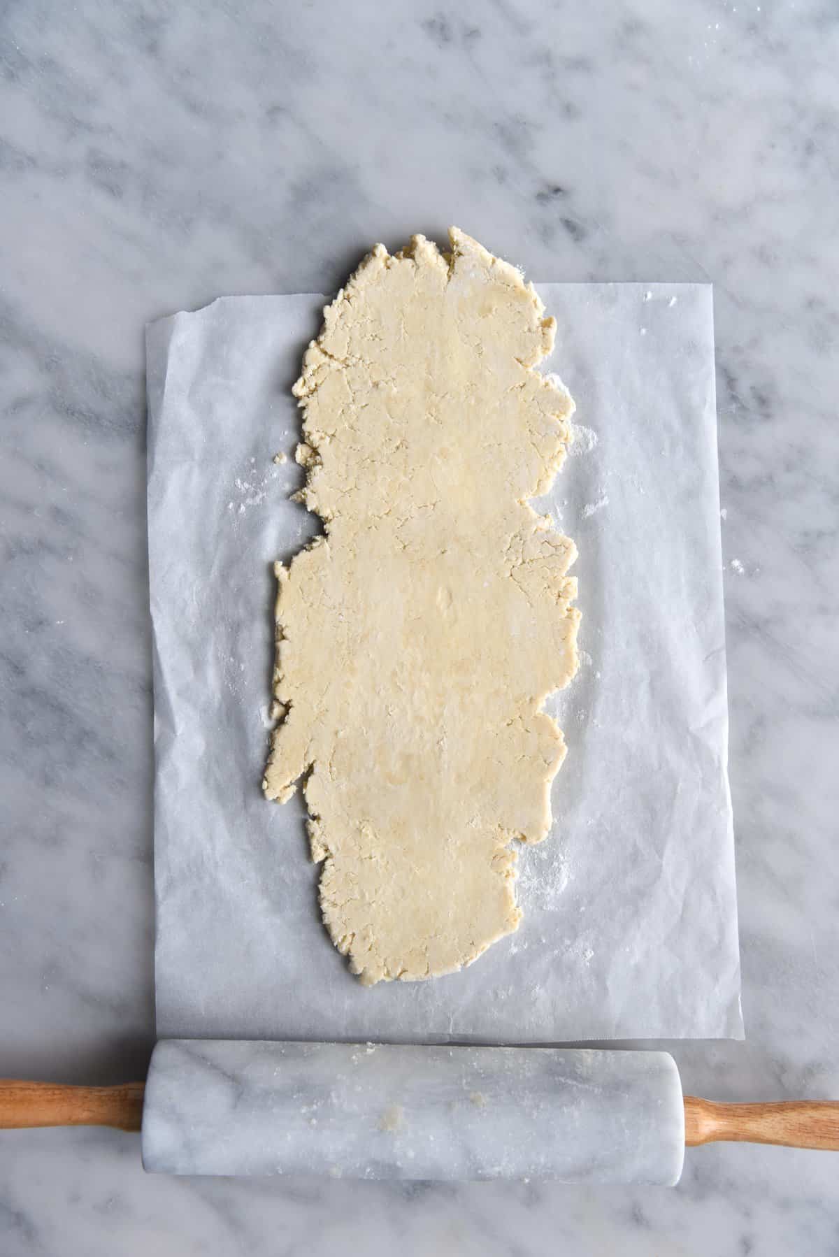 Gluten free butter pastry rolled out on baking paper on a white marble backdrop