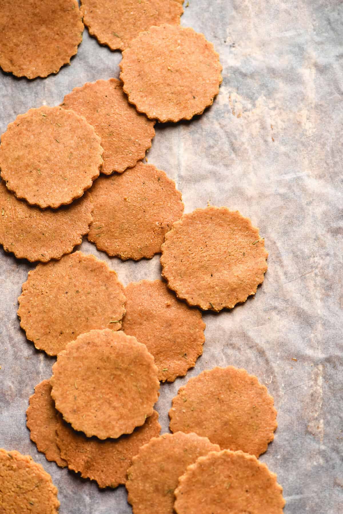 An aerial image of a lined baking tray topped with paleo almond crackers. The crackers are casually arranged and have fluted edges. 