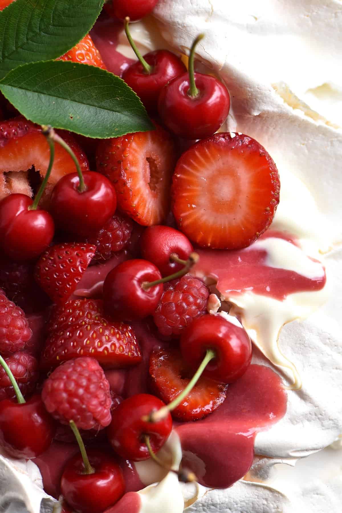 An aerial macro image of a pavlova topped with raspberry curd and fresh berries.