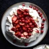 Pavlova covered in lactose free raspberry curd and lots of red berries against a black backdrop