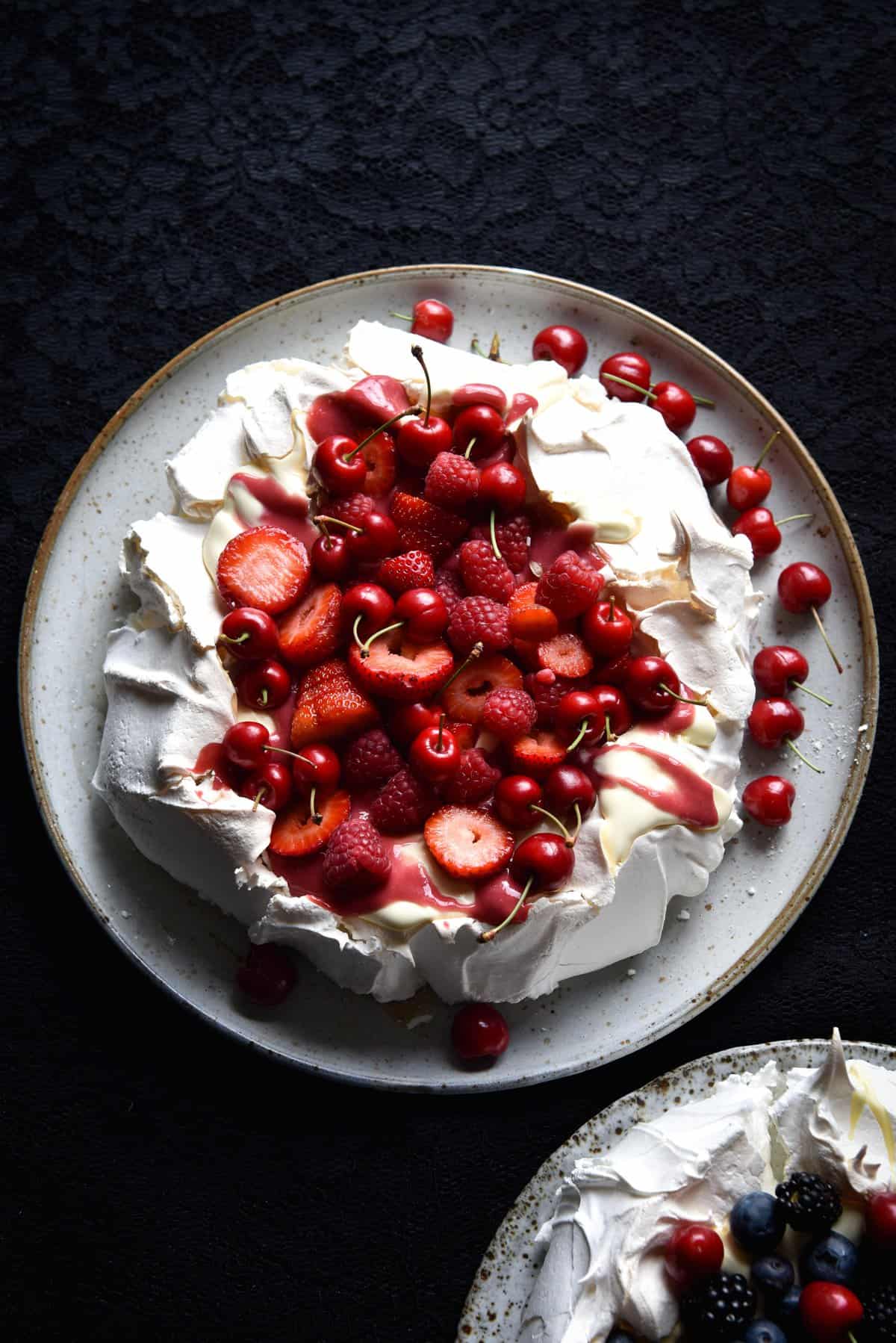 Pavlova covered in lactose free raspberry curd and lots of red berries against a black backdrop
