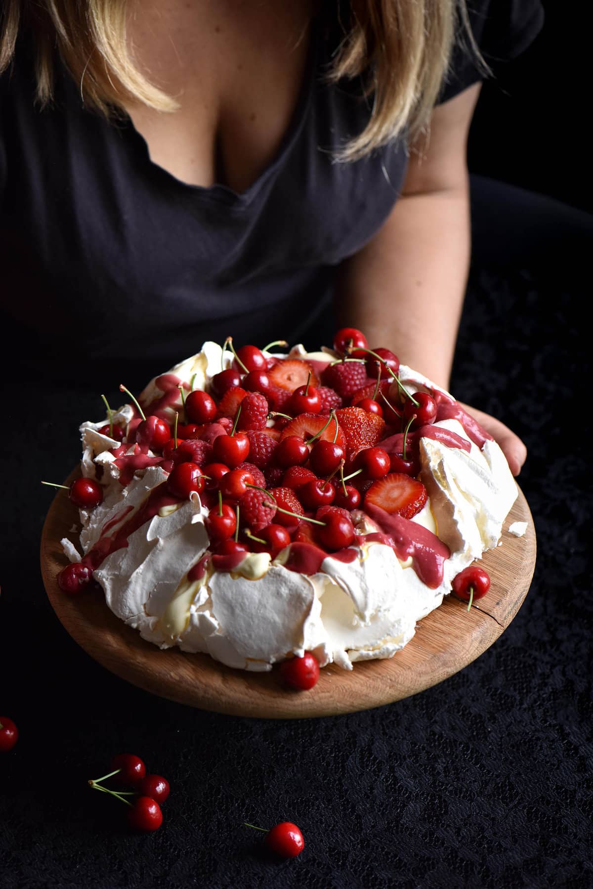 Pavlova with raspberry curd and lots of red berries against a dark backdrop