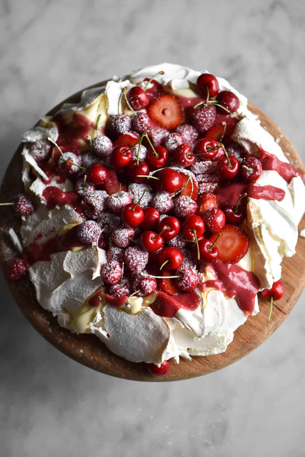 Pavlova with lactose free raspberry yolk curd, berries and cream on a white marble backdrop