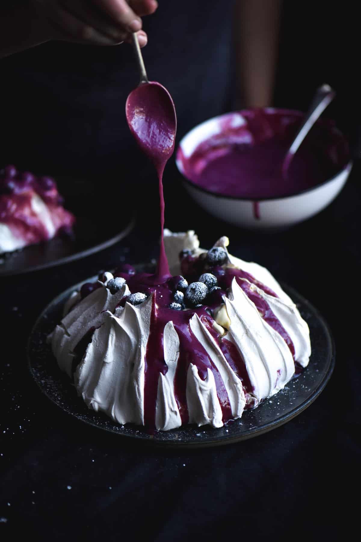 A tall pavlova topped with blueberries and a drizzle of lactose free blueberry curd