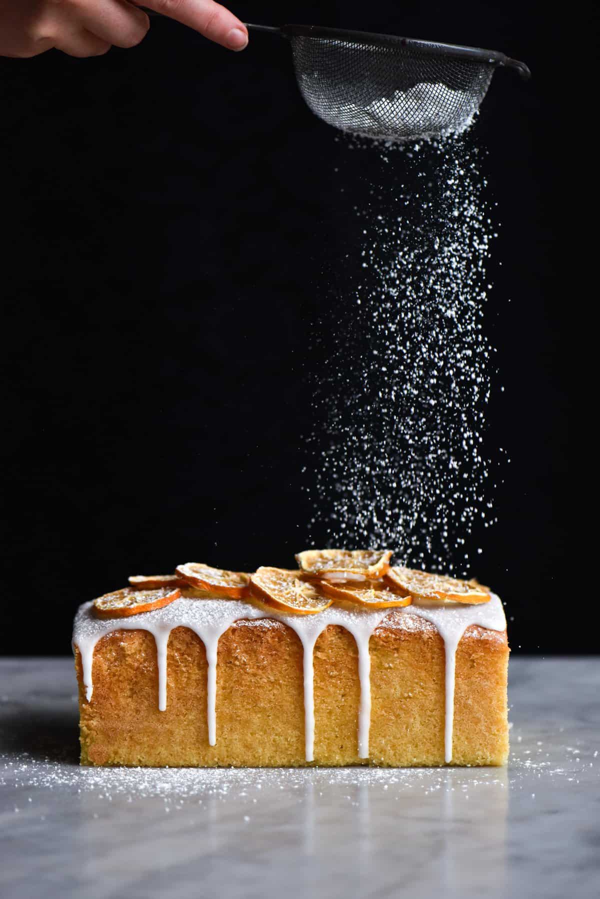 A side on view of a gluten free lemon drizzle cake being sprinkled with icing sugar