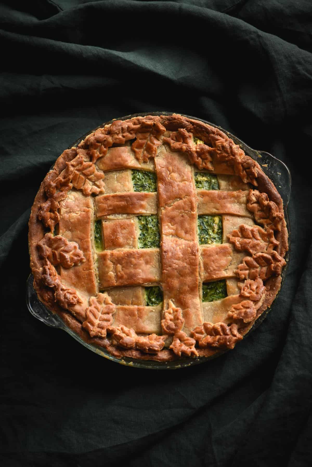 A gluten free greens and feta pie with pastry latticing and decorative pastry leaves against a dark green backdrop