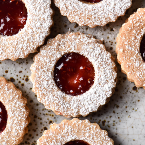Gluten free linzer cookies against a white ceramic backdrop