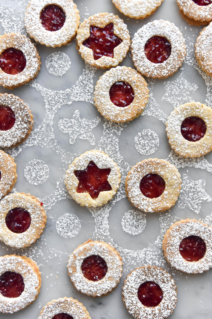 Gluten free linzer cookies dusted with icing sugar against a marble backdrop