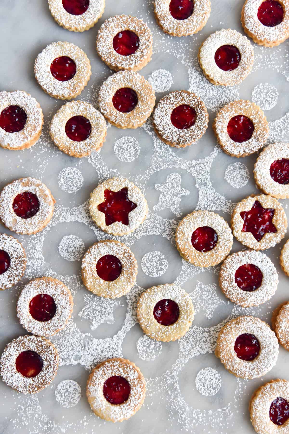 Gluten free linzer cookies dusted in icing sugar on a marble backdrop
