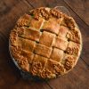 A gluten free curried vegetable pie with a pastry lattice and decorative leaf pie lid, set against a wooden backdrop