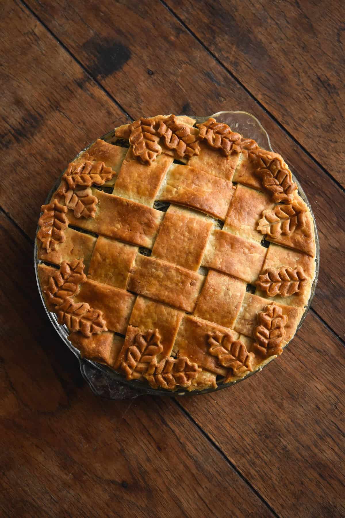 A gluten free curried vegetable pie with a pastry lattice and decorative leaf pie lid, set against a wooden backdrop