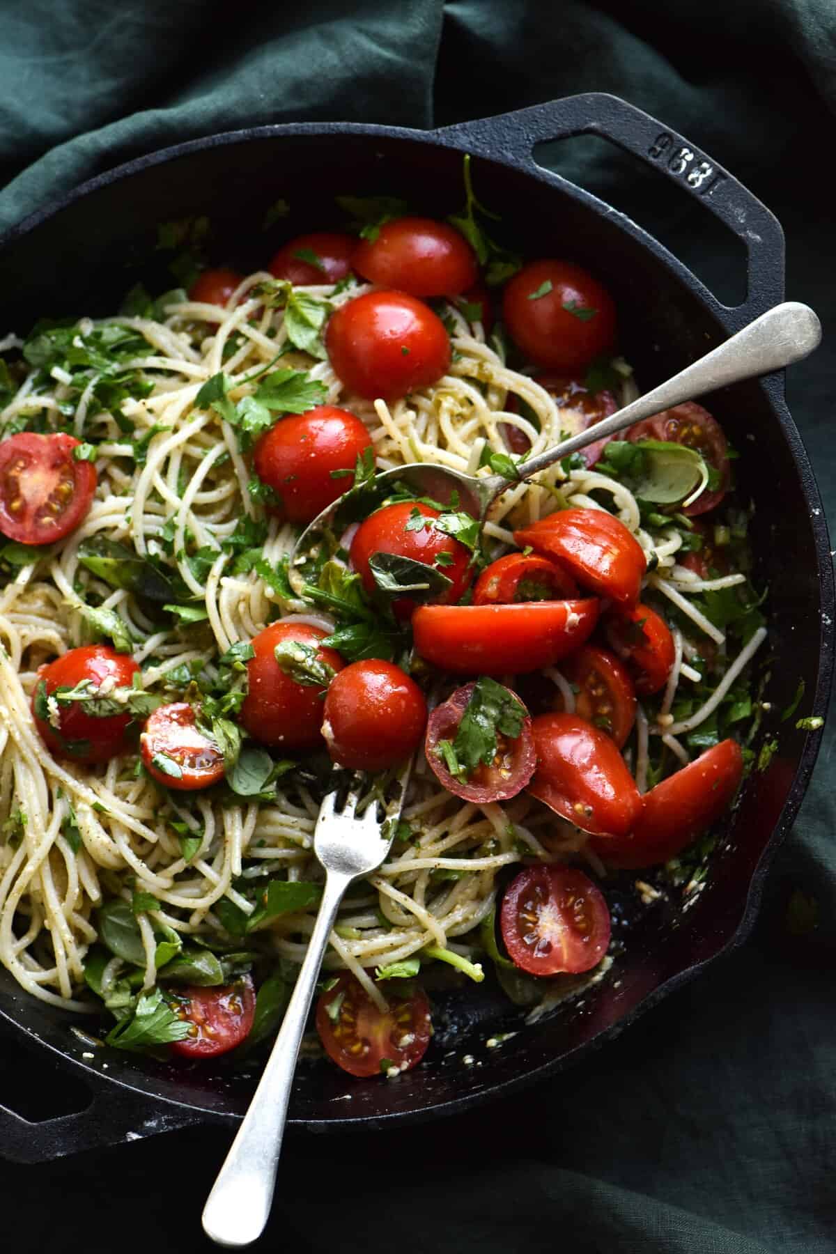 Gluten free pasta with a brown butter, herb, chilli and lemon dressing, topped with fresh summer tomatoes. Served in a skillet set against an olive green linen tablecloth