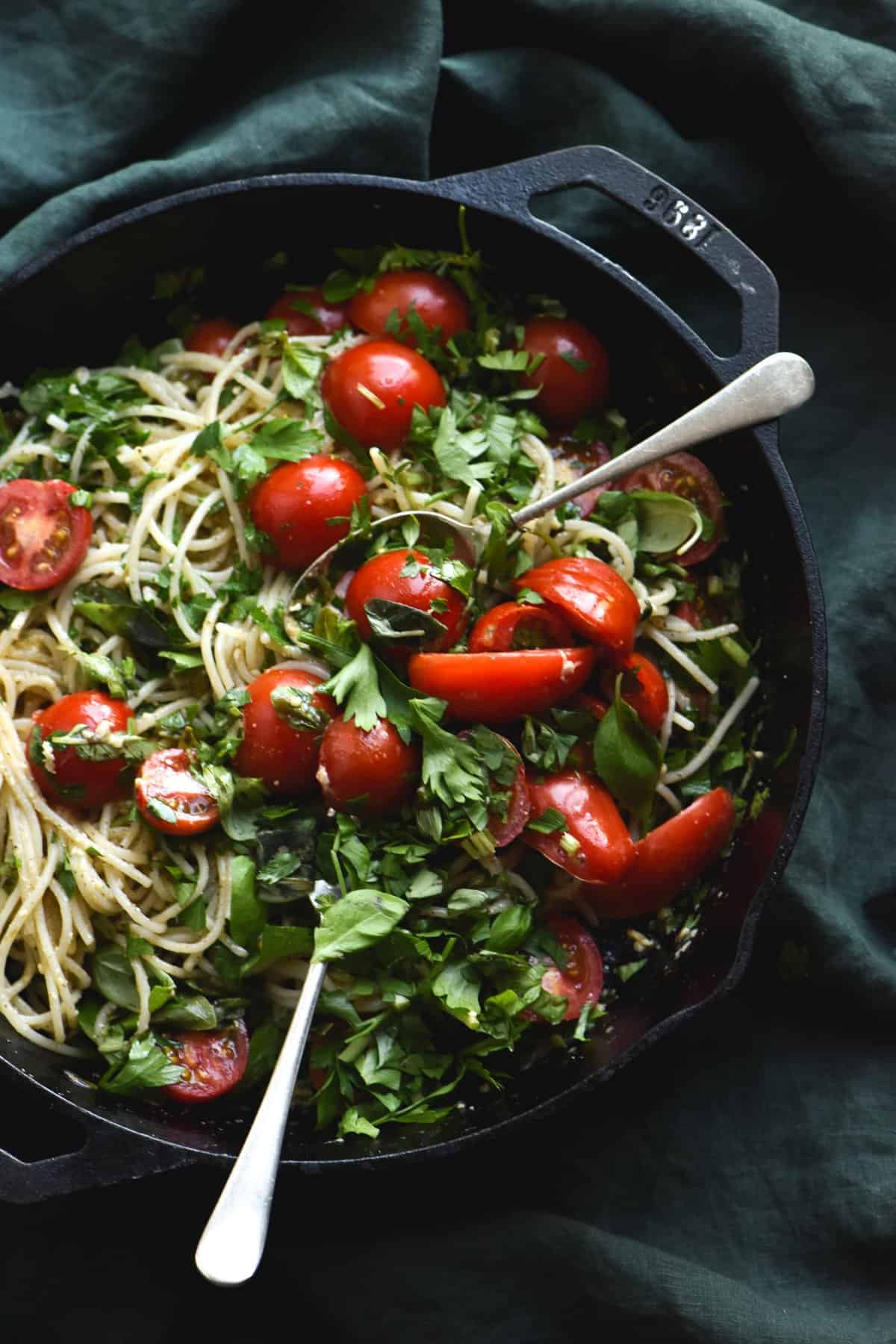 Gluten free pasta with a brown butter, herb, chilli and lemon dressing, topped with fresh summer tomatoes. Served in a skillet set against an olive green linen tablecloth