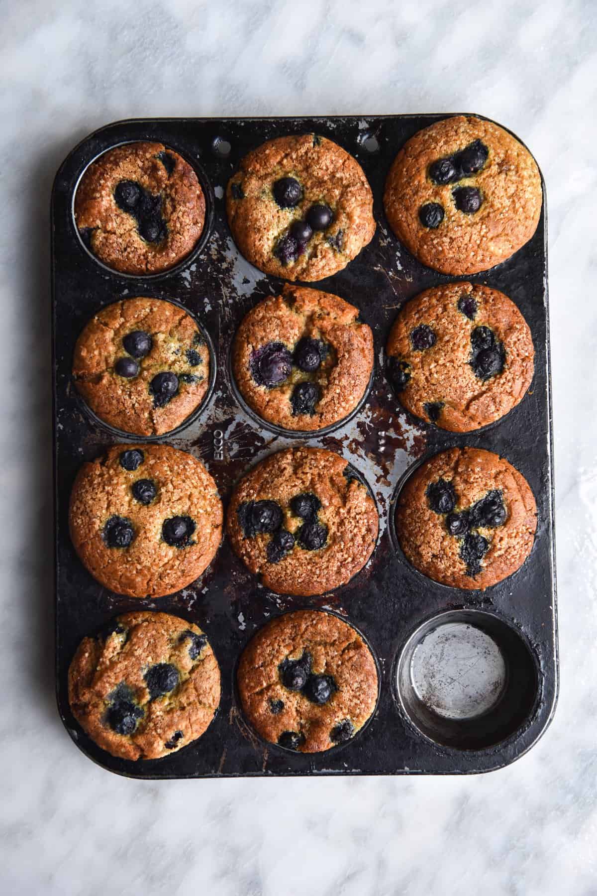 A tray of vegan, gluten free blueberry muffins against a white marble backdrop