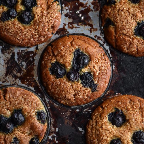 A close up of some vegan, gluten free blueberry muffins in a rustic muffin tray