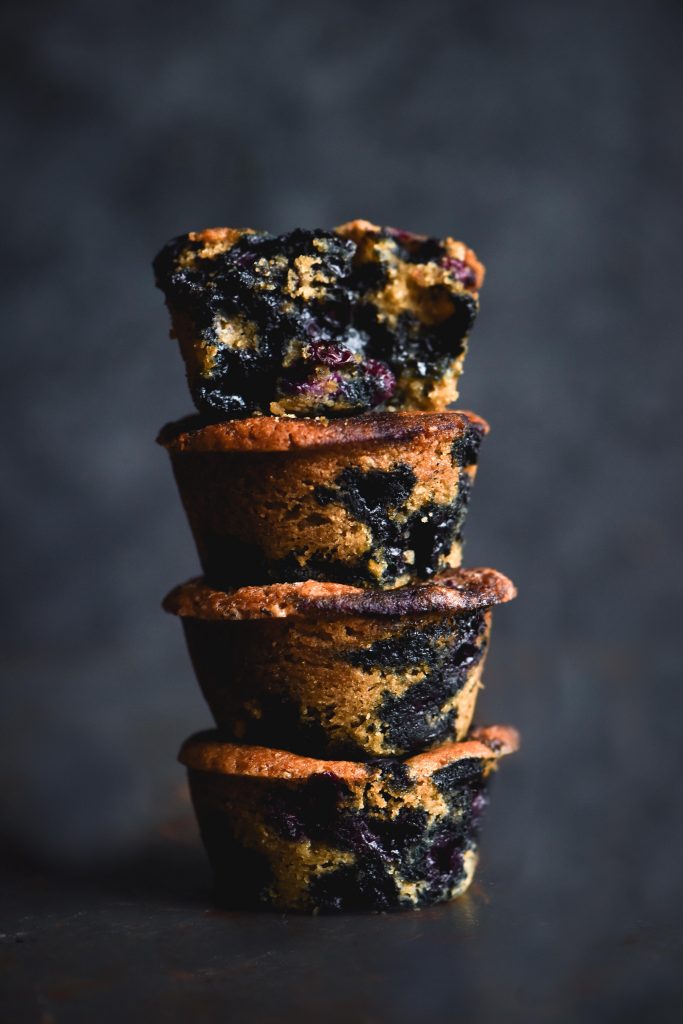 A stack of blueberry filled vegan, gluten free muffins against a mottled blue backdrop