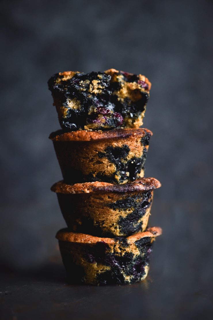 A stack of blueberry filled vegan, gluten free muffins against a mottled blue backdrop