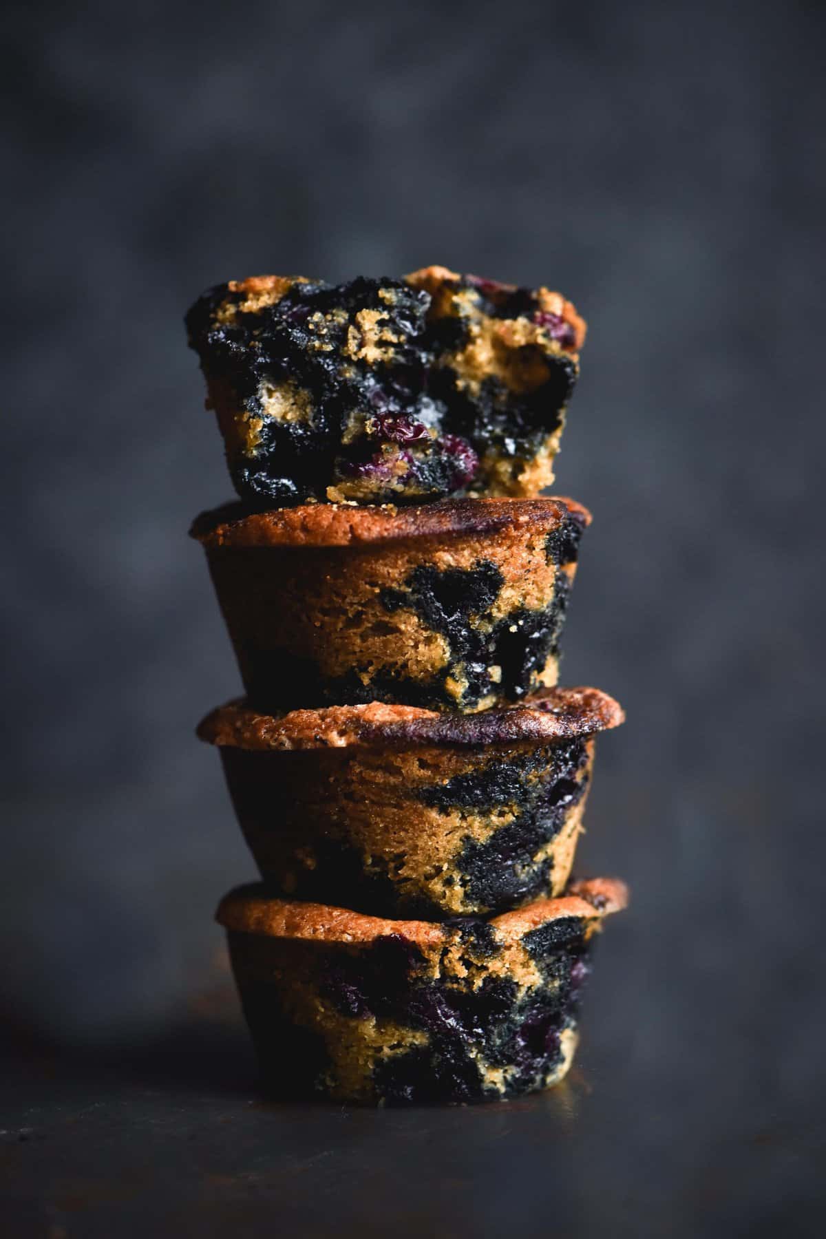 A stack of blueberry filled gluten free egg free muffins against a mottled blue backdrop