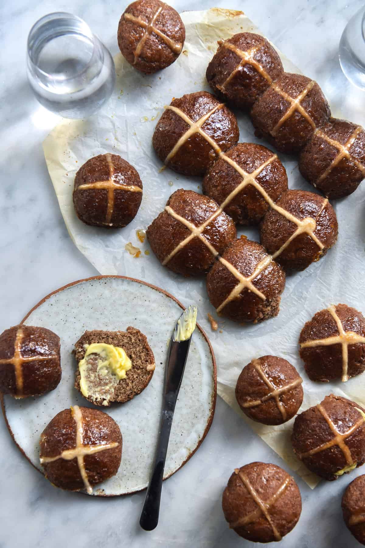 Gluten free, FODMAP friendly and vegan hot cross buns strewn across a white marble backdrop