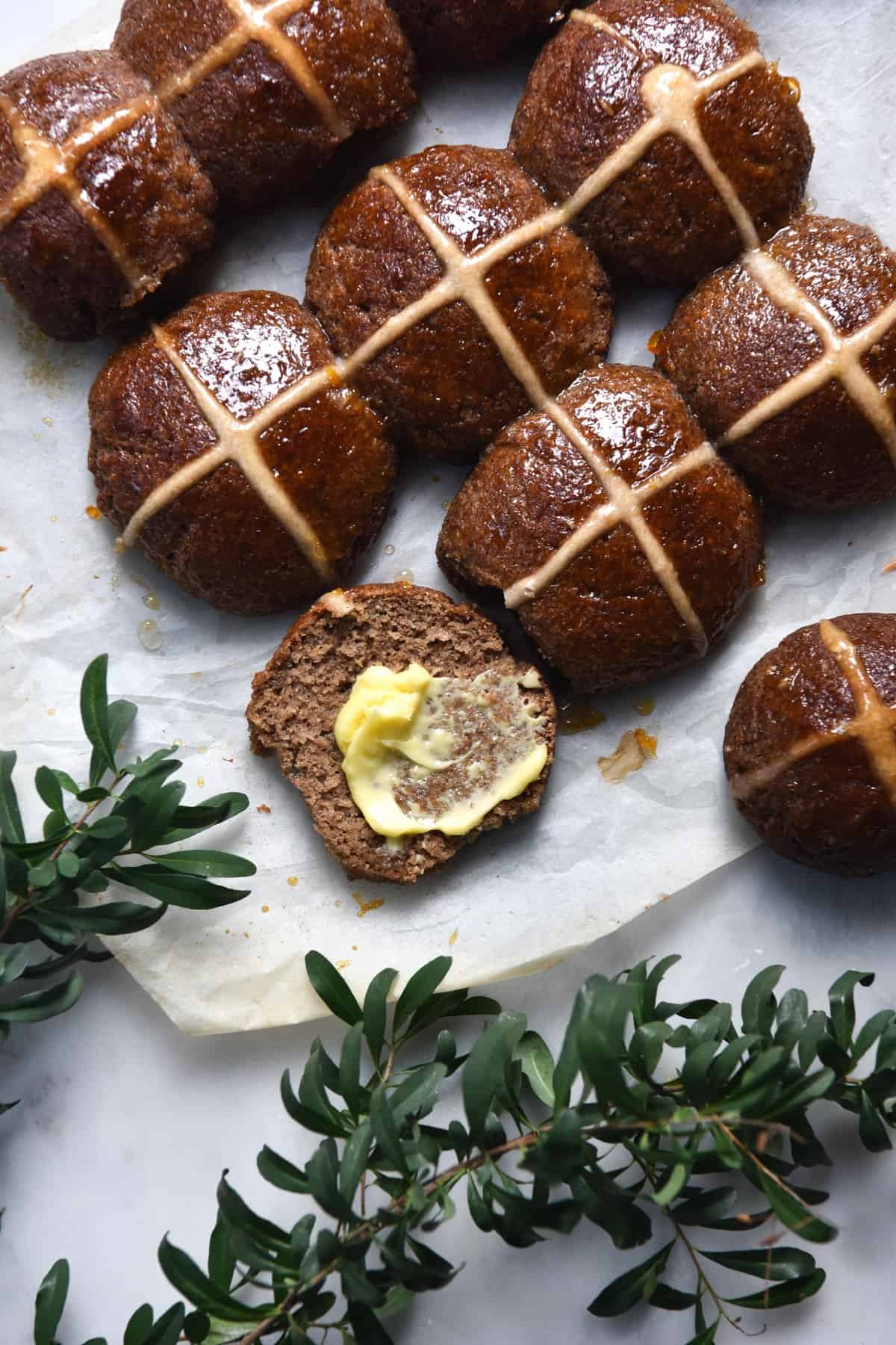 A close up of gluten free, vegan and FODMAP friendly hot cross buns surrounded by green floral leaves