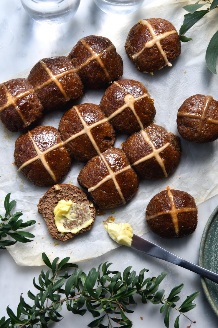 Gluten free, vegan and FODMAP friendly hot cross buns against a white marble backdrop surrounding by green florals