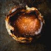 A burnt Basque style mini cheesecake sprinkled with icing sugar against a mottled metallic backdrop