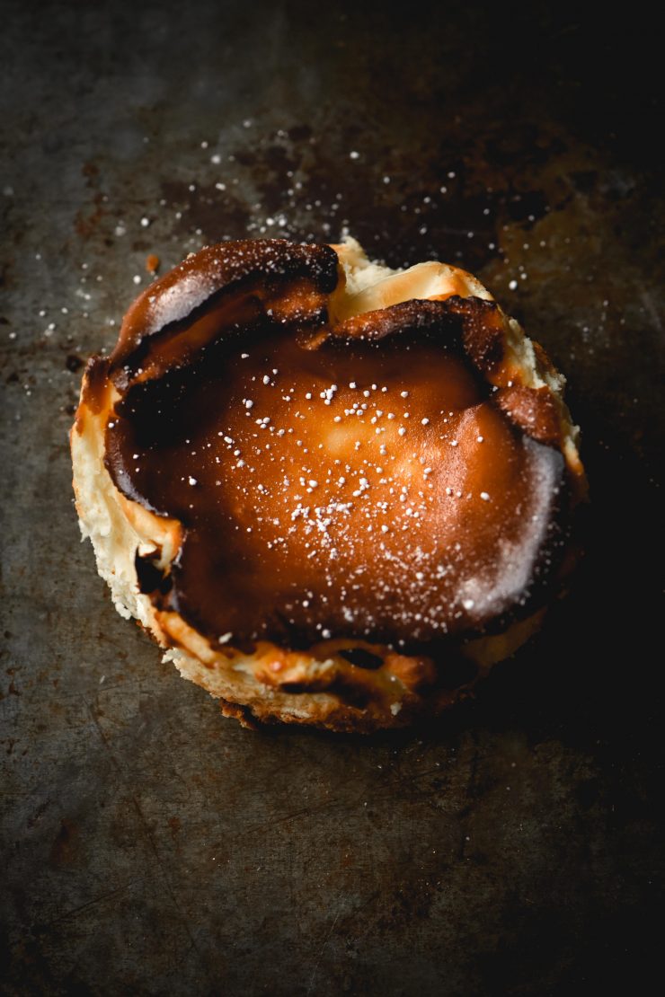 A burnt Basque style mini cheesecake sprinkled with icing sugar against a mottled metallic backdrop