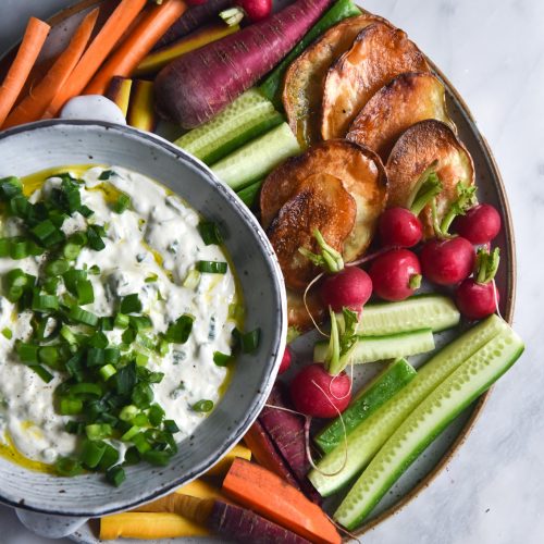 An aerial shot of a bowl of FODMAP friendly spring onion dip set amongst a plate of brightly coloured crudites