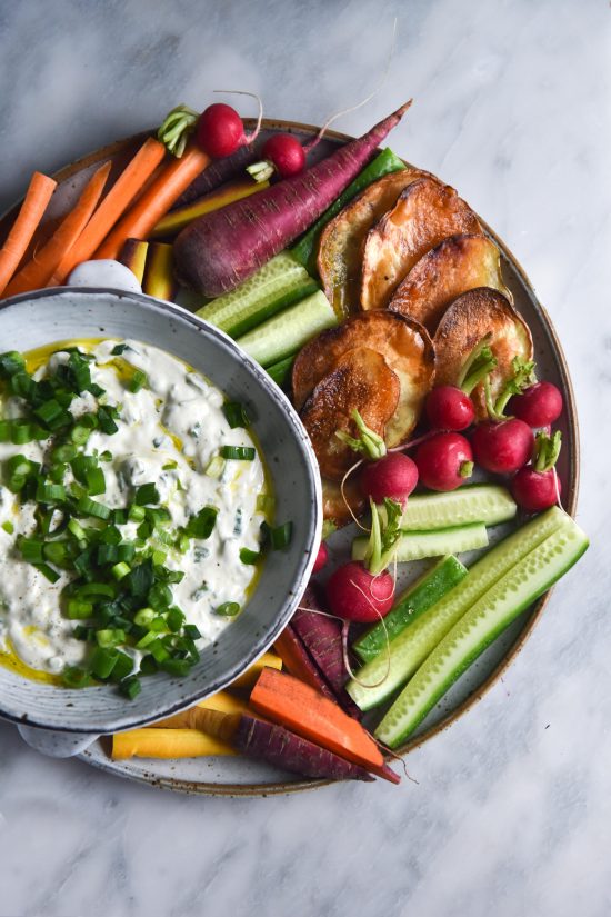 An aerial shot of a bowl of FODMAP friendly spring onion dip set amongst a plate of brightly coloured crudites